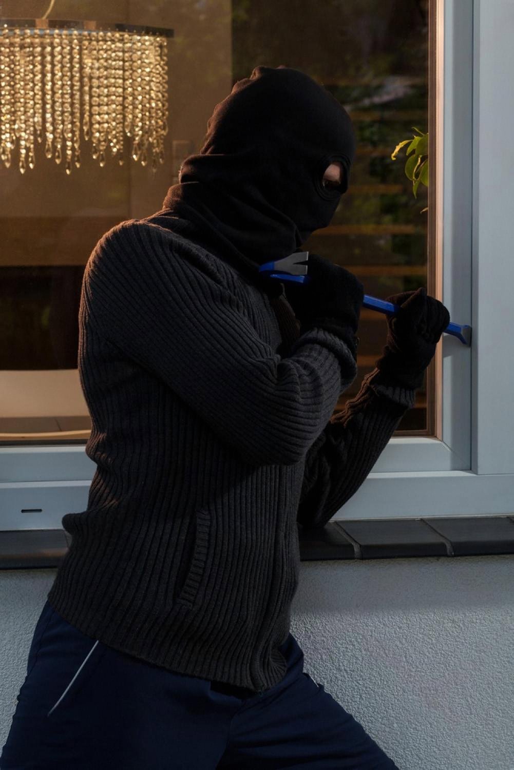 Masked intruder using a crowbar to pry open a ground-floor window at night