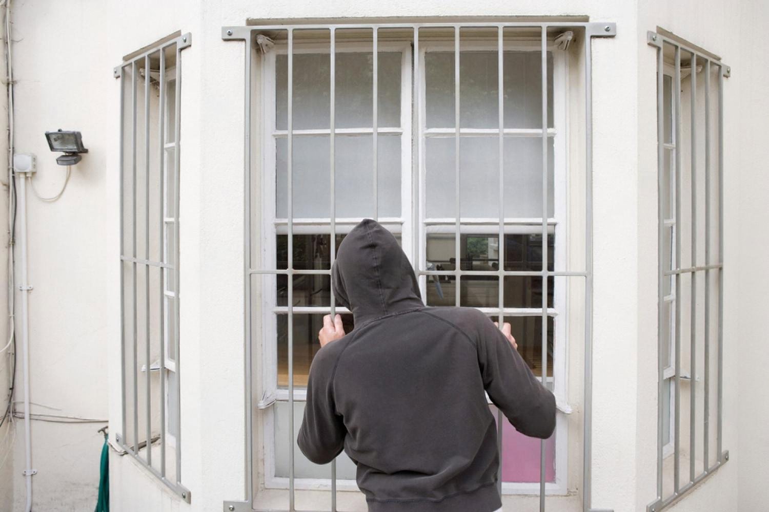 Hooded person testing steel security bars fitted over a ground-floor window